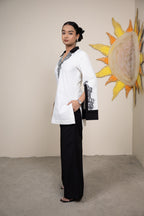Woman in a white and black outfit standing in front of a wall with a sun and shell decoration.
