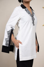 White tunic with black embroidery on a plain background