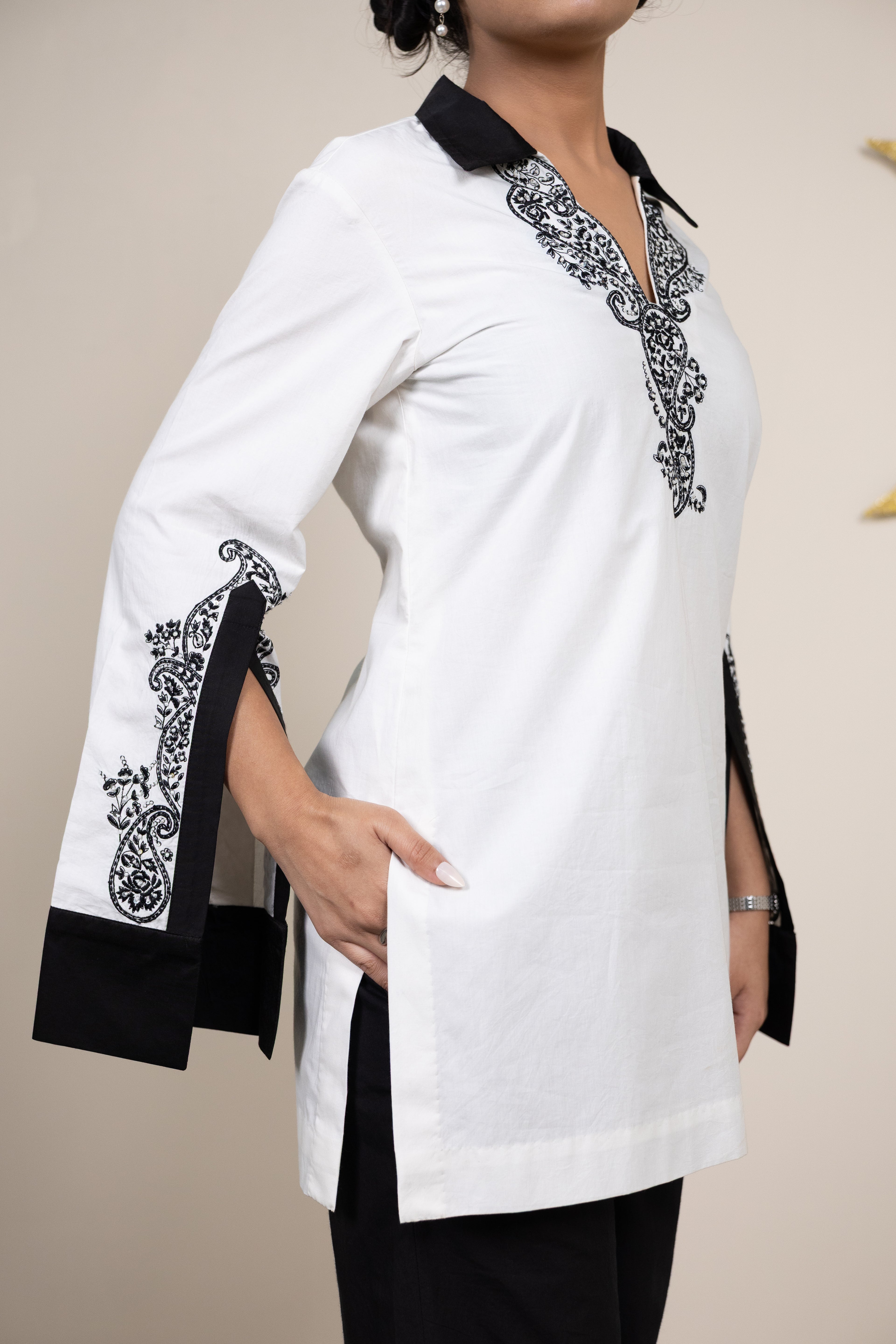 White tunic with black embroidery on a plain background