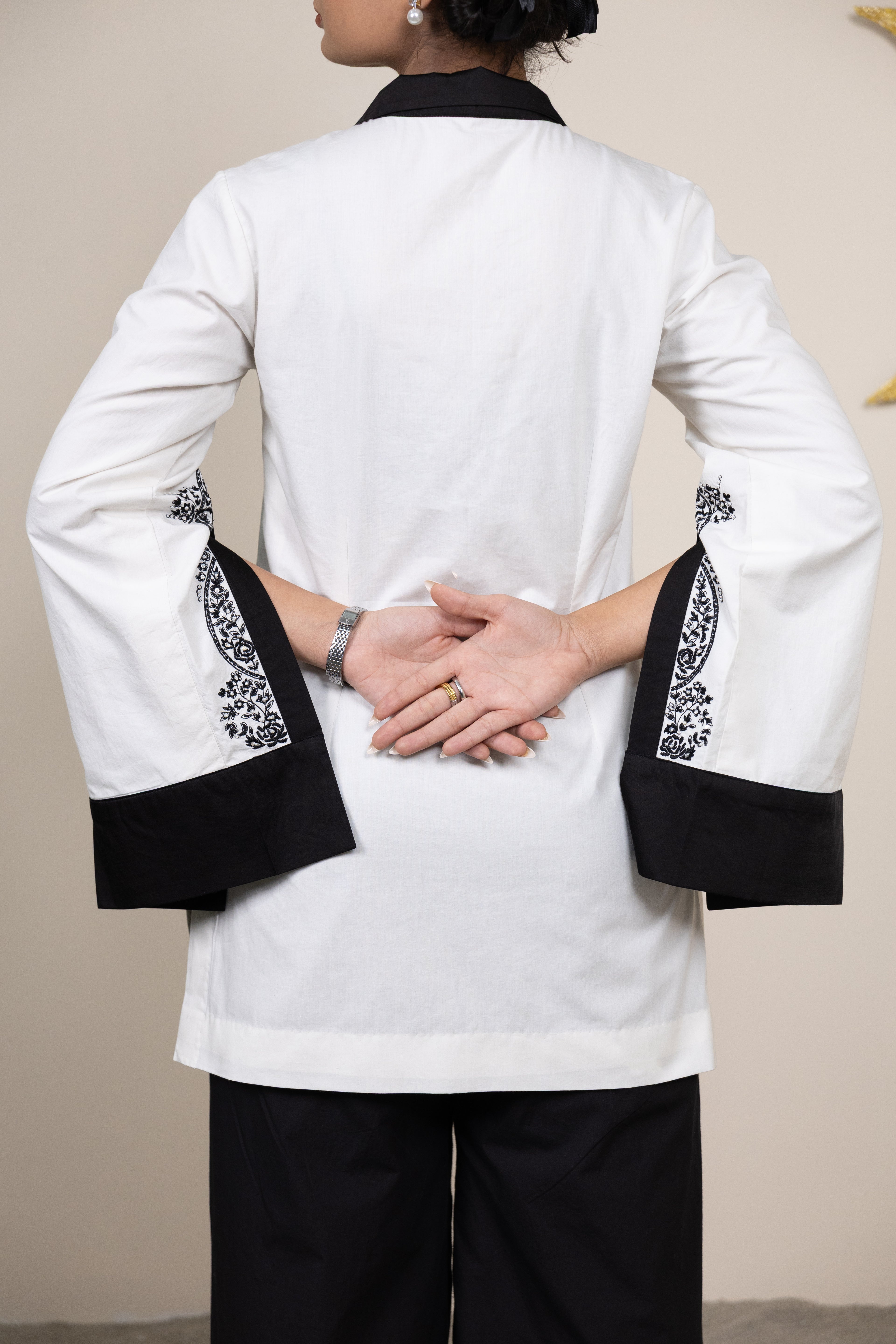 Person wearing a white jacket with black and white patterned cuffs on a beige background