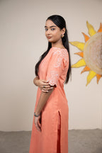 Woman in a peach outfit with floral embroidery standing in front of a sun mural.