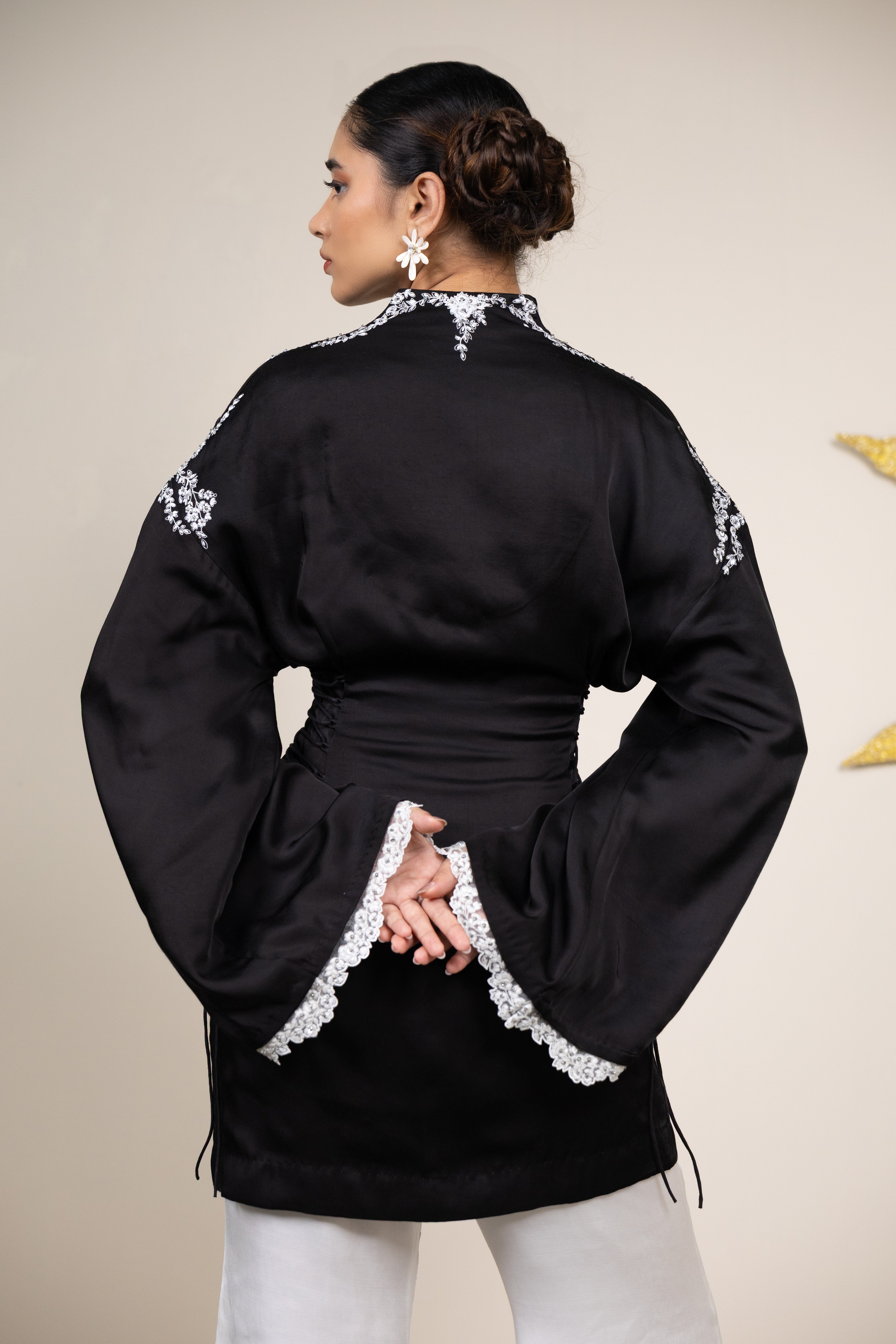 Woman wearing a black embroidered jacket with white trim on a beige background