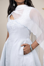 White dress with sheer overlay worn by a person, against a neutral background