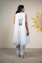 Woman in a white outfit standing in front of a sun mural on a beige wall.