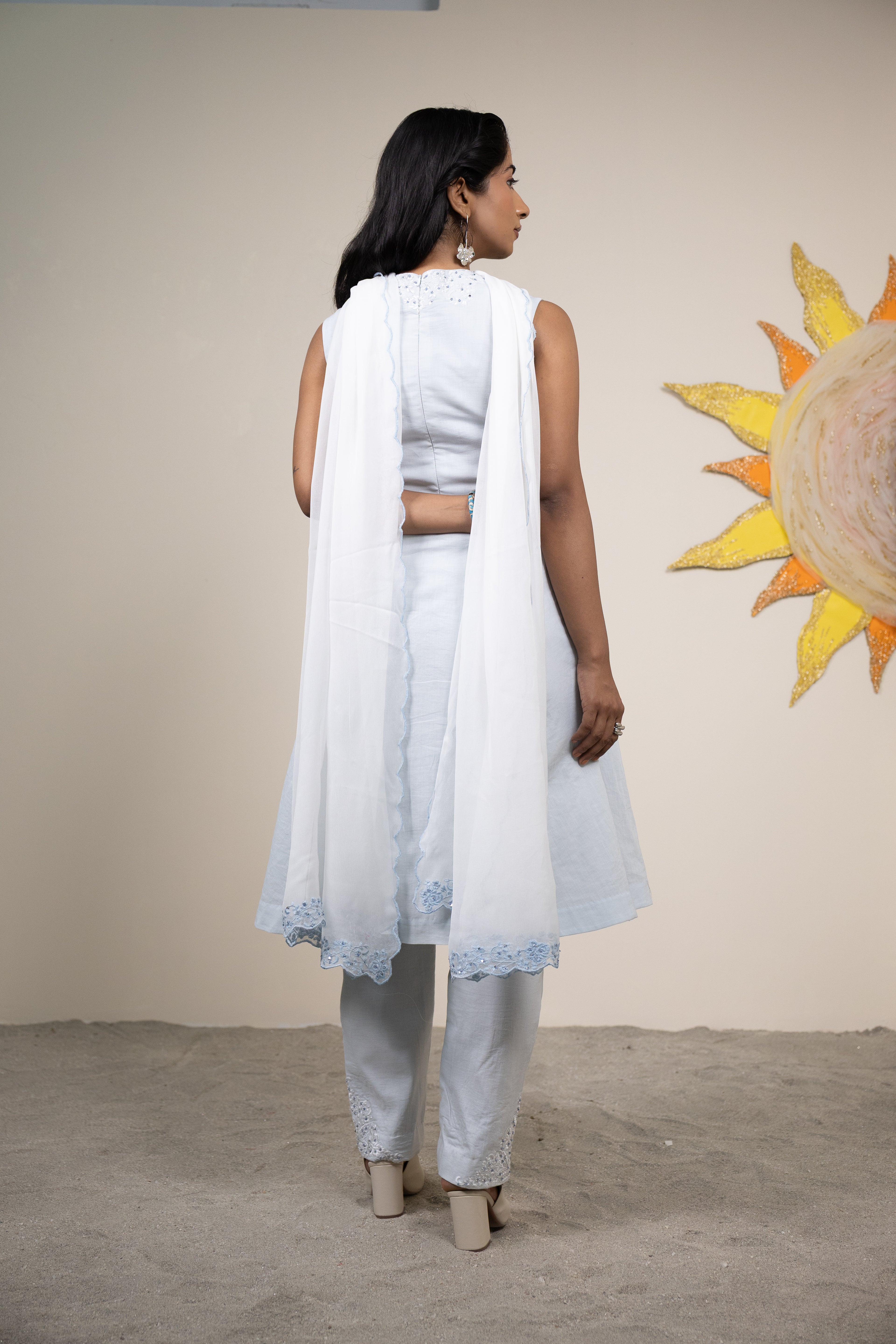 Woman in a white outfit standing in front of a sun mural on a beige wall.