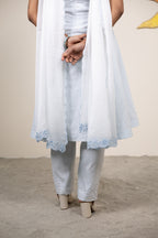 Person wearing a white outfit with lace details on a plain background
